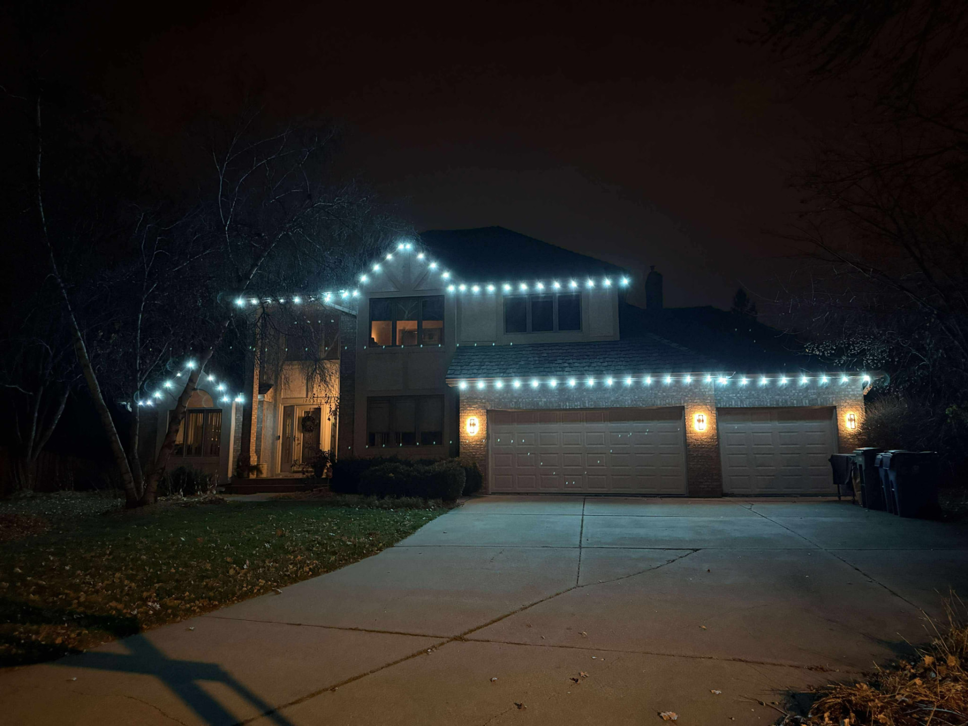 Night install with bright cool white roofline lights and warm entry sconces
