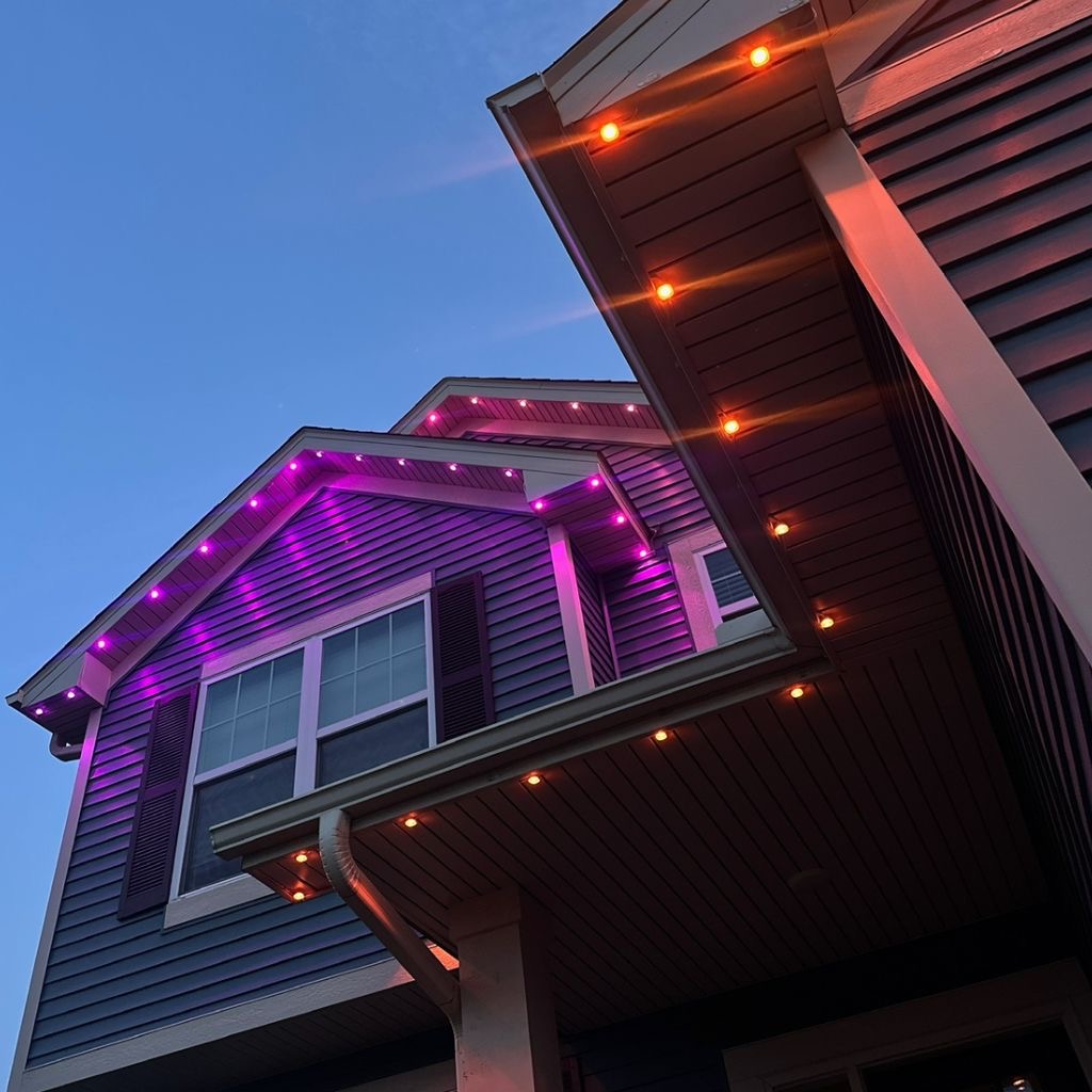 Close-up of soffit downlights washing the eaves in magenta and warm amber at dusk