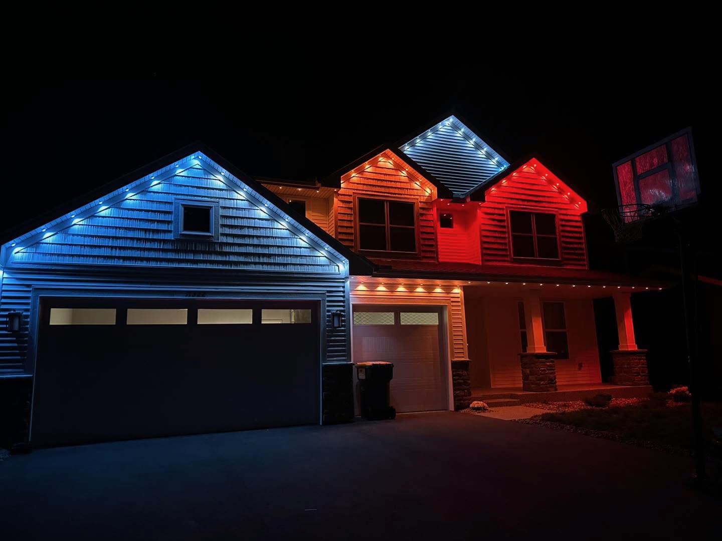 Multi-gable home with blue, cool white, amber, and red roofline lighting at night